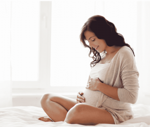Pregnant women gently holding stomach and gazing down at belly